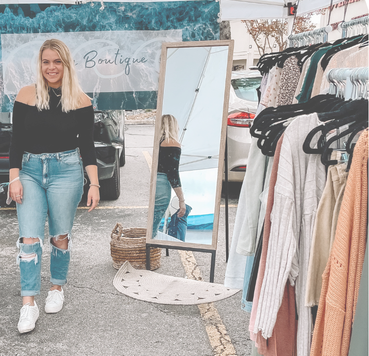 Woman shopping at an outdoor market with a tent and clothing racks.