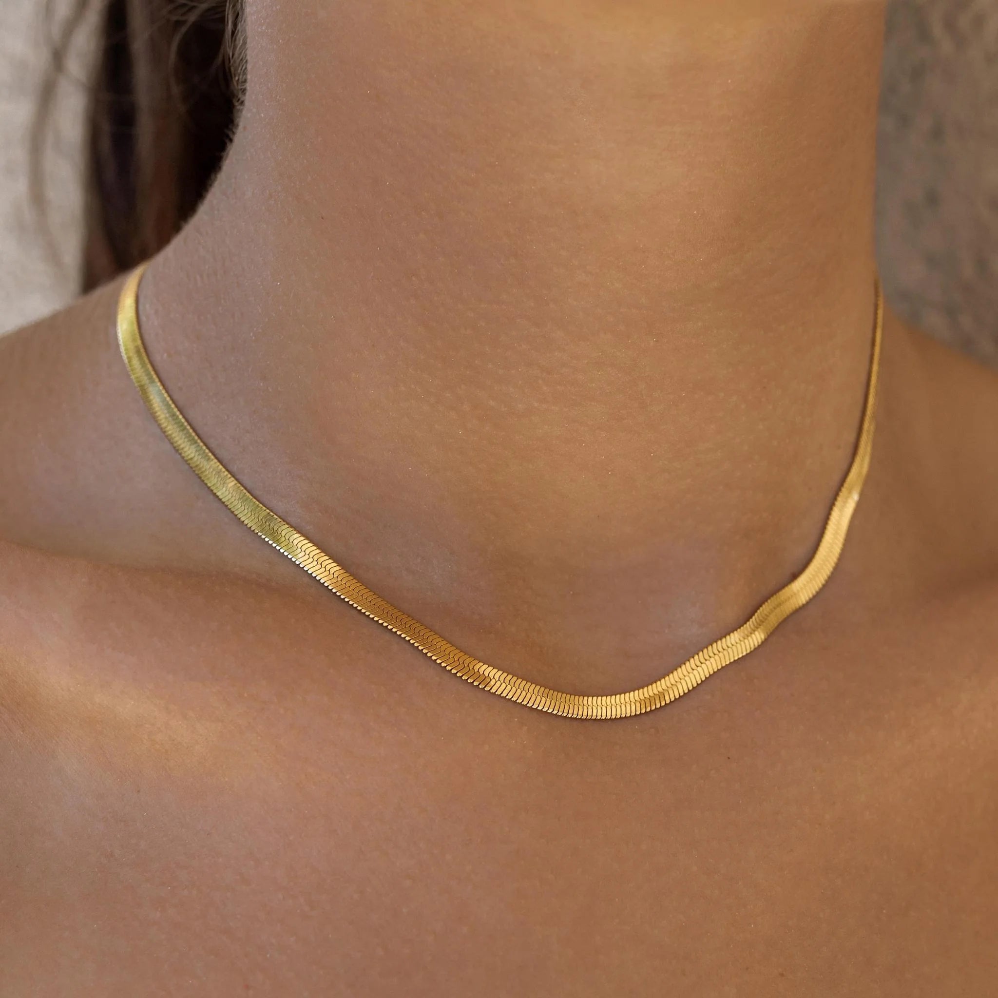 Gold necklace on a person's neck with a neutral background
