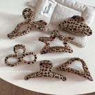 A collection of leopard print claw hair clips of various sizes displayed on a white surface with a leopard print bag in the background.