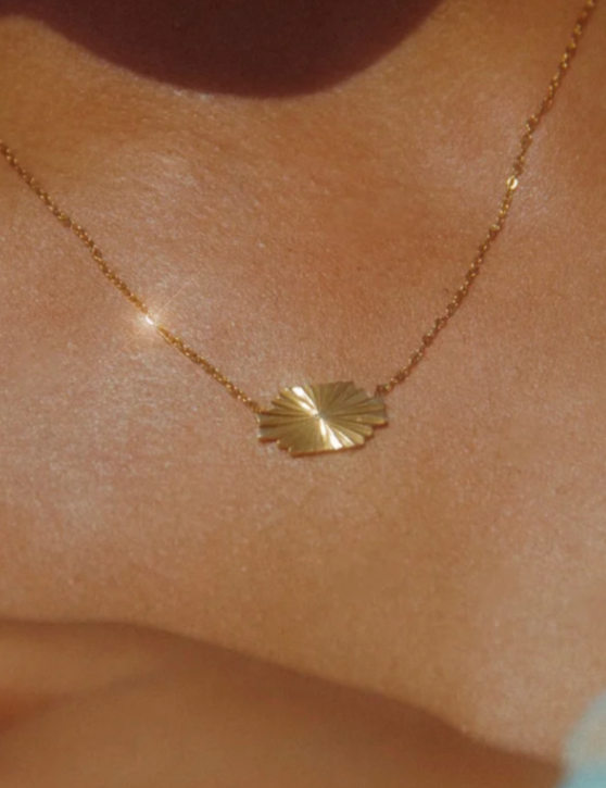 Gold necklace with a leaf pendant on a person's neck