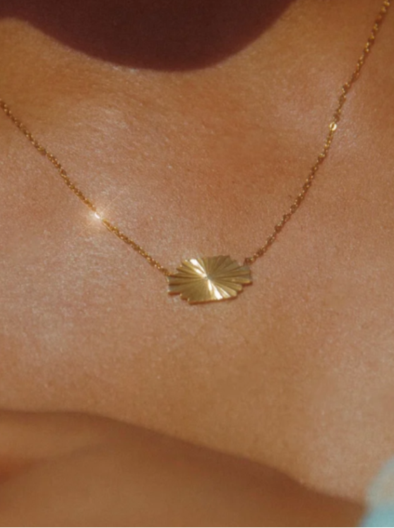 Gold necklace with a leaf pendant on a person's neck