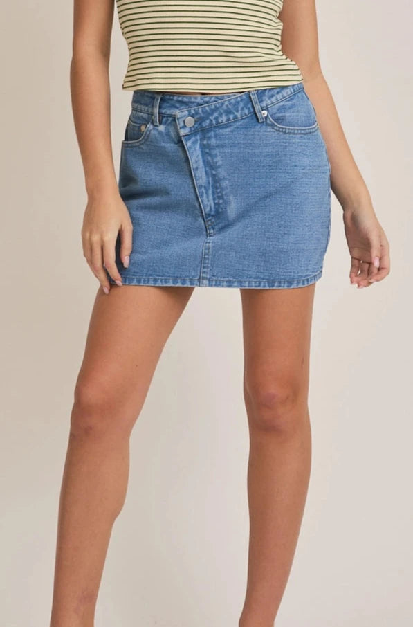 A medium wash denim skort with a crossover waist and built-in shorts, worn by a model.