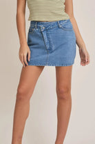 A medium wash denim skort with a crossover waist and built-in shorts, worn by a model.
